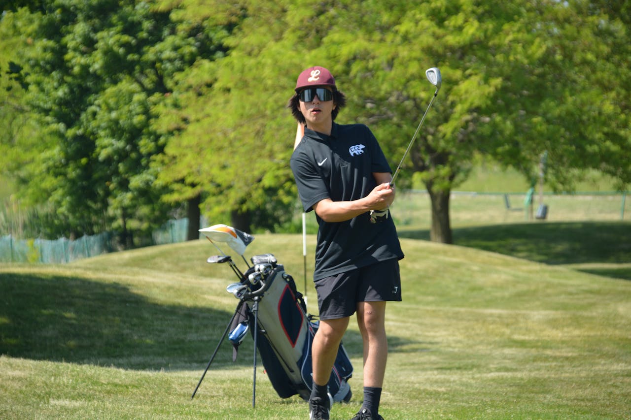 Teen golfer in action on a sunny day in the park, showcasing technique with golf club.