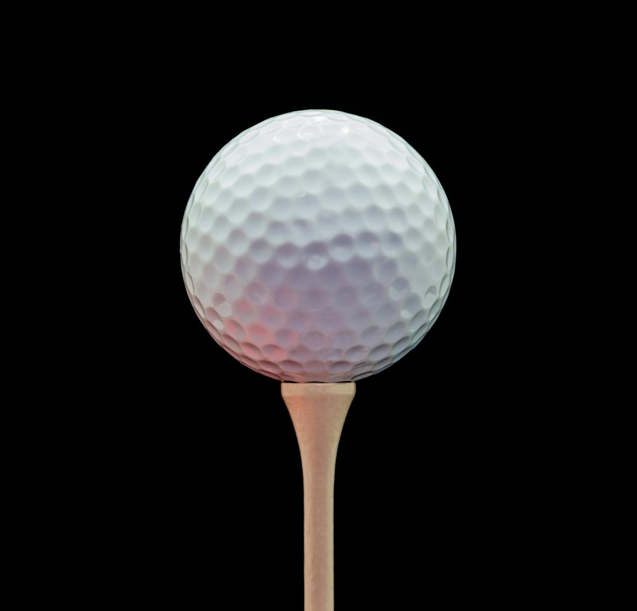 Close-up of a golf ball on a tee against a black background, showcasing texture and detail.